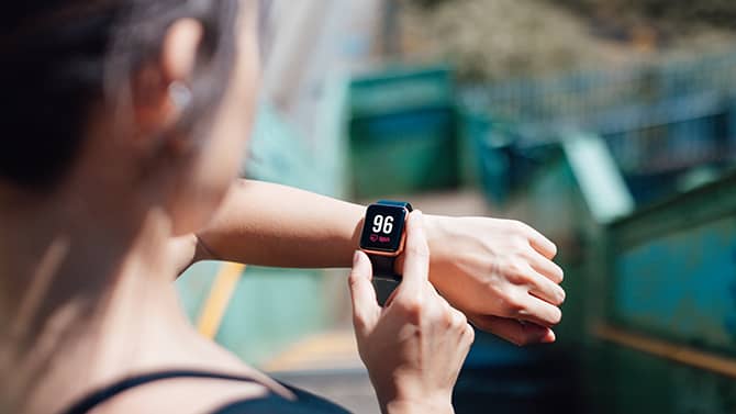 A woman uses a fitness app on her phone, synced to a wearable monitoring device on her wrist.